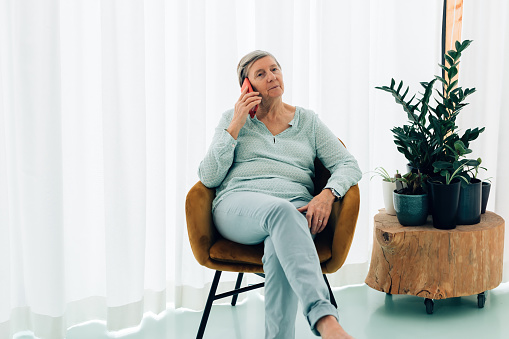senior woman sitting at home having phone conversation using smartphone