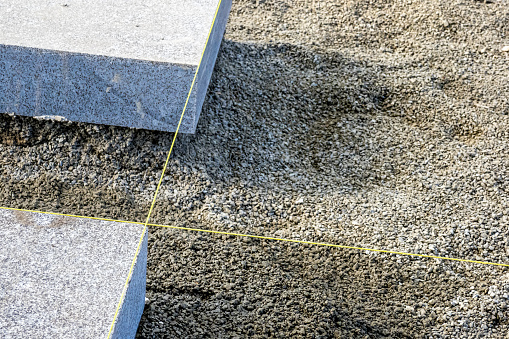 A yellow nylon string marking the alignment for accurately laid solid granite blocks on the gravel surface of a construction site, creating a perfect walkway with copy space on the right side.