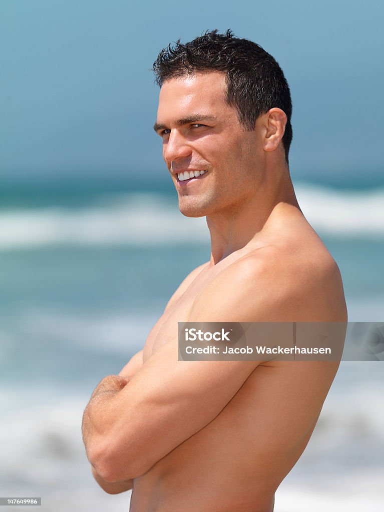 Bonito jovem homem de pé com os braços cruzados na praia - Foto de stock de 20 Anos royalty-free