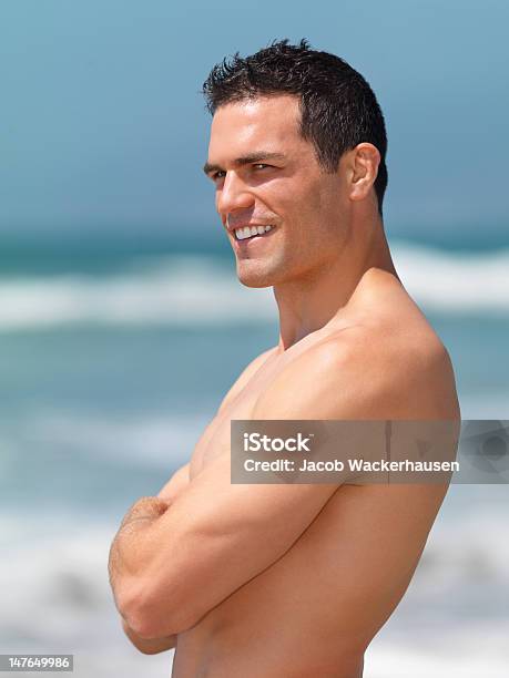 Foto de Bonito Jovem Homem De Pé Com Os Braços Cruzados Na Praia e mais fotos de stock de 20 Anos