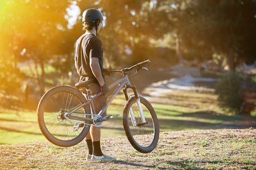 Bike, fitness and summer with a sports man outdoor in nature for leisure or recreation in summer. Back, bicycle and exercise with a male athlete standing on an open green field carrying his transport