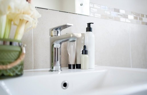 Different toiletries bottles and tubes on white bathroom sink at home