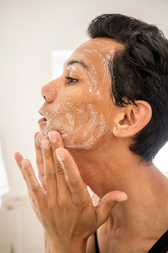 Close-up of a mid adult person washing their face with foam in bathroom