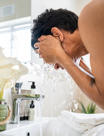 Close-up of a mid adult person washing their face at the bathroom sink with water running from faucet