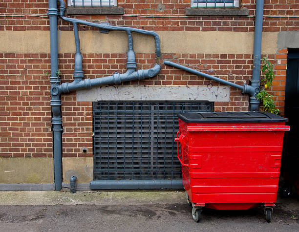Red garbage bin and outside sewer pipes stock photo