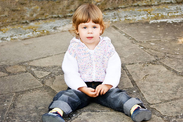 Little girl in knitted casual coat sitting on the ground.