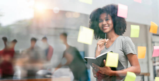 istock Young smiley attractive, businesswoman using sticky notes in glass wall to writing strategy business plan to development grow to success 1476531310
