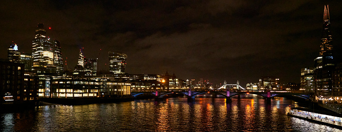 London, United Kingdom - 23 December 2022: Illuminated buildings at night along the River Thames in London, United Kingdom.