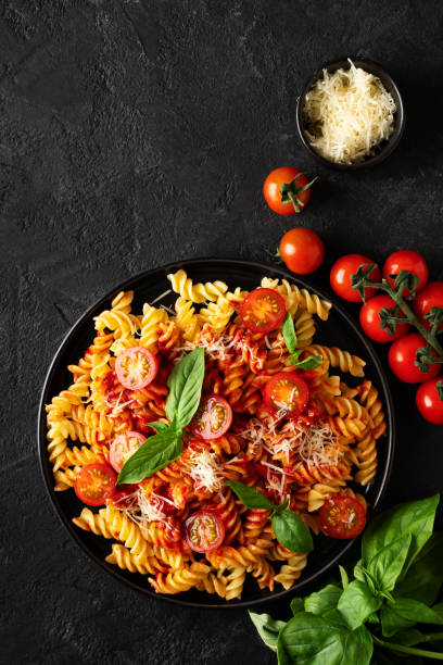istock Fusilli pasta with tomatoes, basil, parmesan, and sauce on back background 1476567932