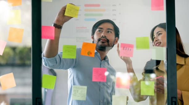 istock Two Creative business people brainstorming writing on sticky notes on glass wall in office 1476569670