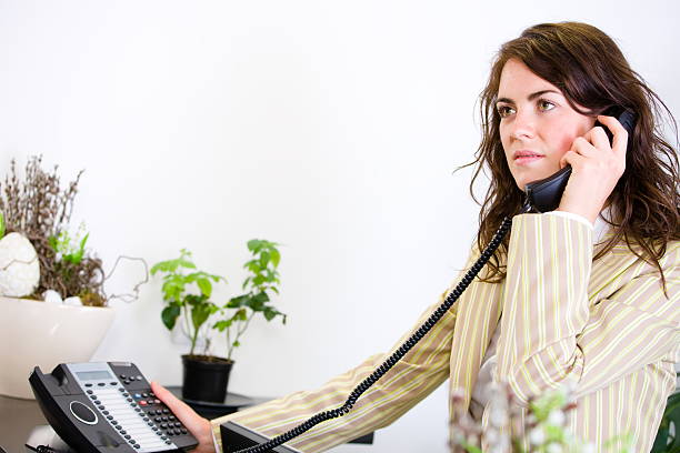 Cute Female Businesswoman sitting in executive class chair and talking on telephone Office interior with many colourful folders computer screen and other items on background