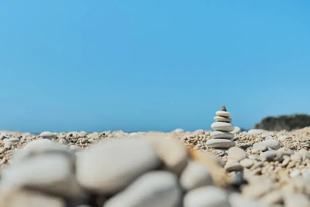 Photo of Pyramid stones balance on the beach against a blue bright sky. Object in focus, blurred background, idea of a vacation or retweet by the sea