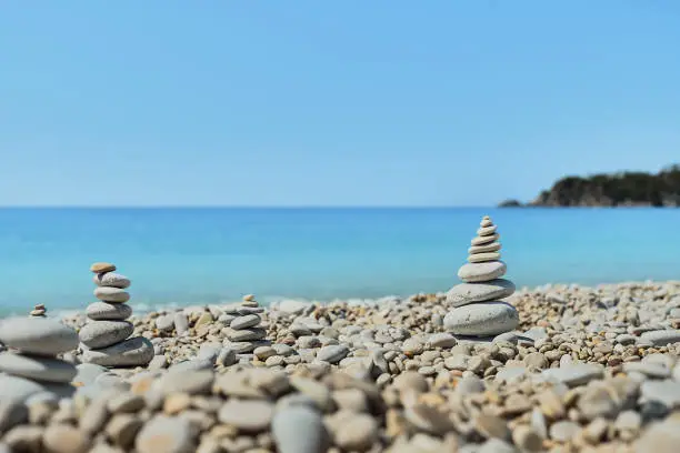 Photo of Pyramid stones balance on the beach against the background of the sea and the sky. Object in focus, blurred background, idea of a vacation or retweet by the sea