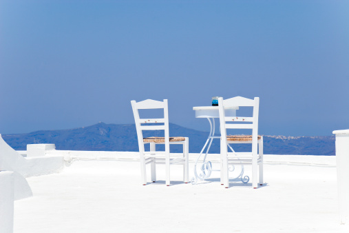 Two chairs with table on a terrace with a view of the Mediterranean, ready for holiday makers. Santorini, Greece.