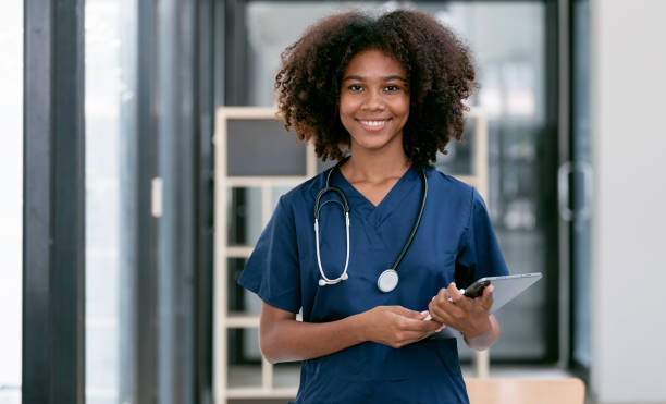 portrait of confident, happy female nurse or doctor with stethoscope and tablet standing in hospital hallway, smiling to camera. - female nurse imagens e fotografias de stock