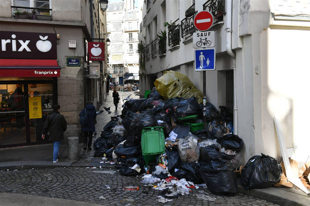 Paris, France-03 24 2023: People passing between the heaps of rubbish that overflow on the sidewalks of Paris, France during the garbage collectors' strike.