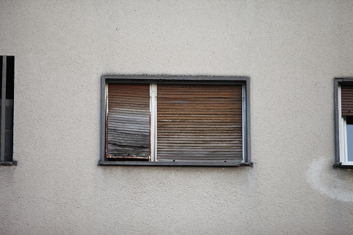 Closed old brown blind on a window, on a building with a white facade
