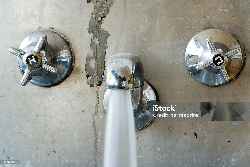 grungy tap gushing water; close crop Dirty tap or faucet gushing water at fully open. Possibly representing water wastage. Part of a series. Shot taken in a classroom at a stainless steel washing trough. Bathroom Stock Photo