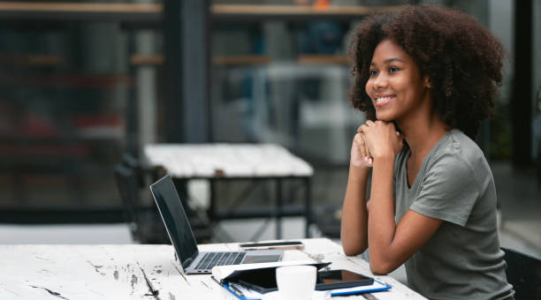 istock Smiling African American woman sitting at co-workspace looking away while working. 1476592570
