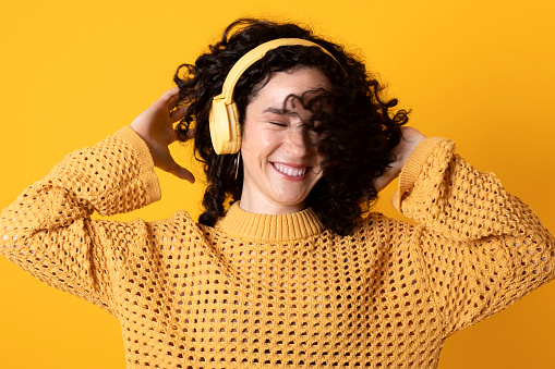 Curly black-haired girl dancing with headphones on yellow background