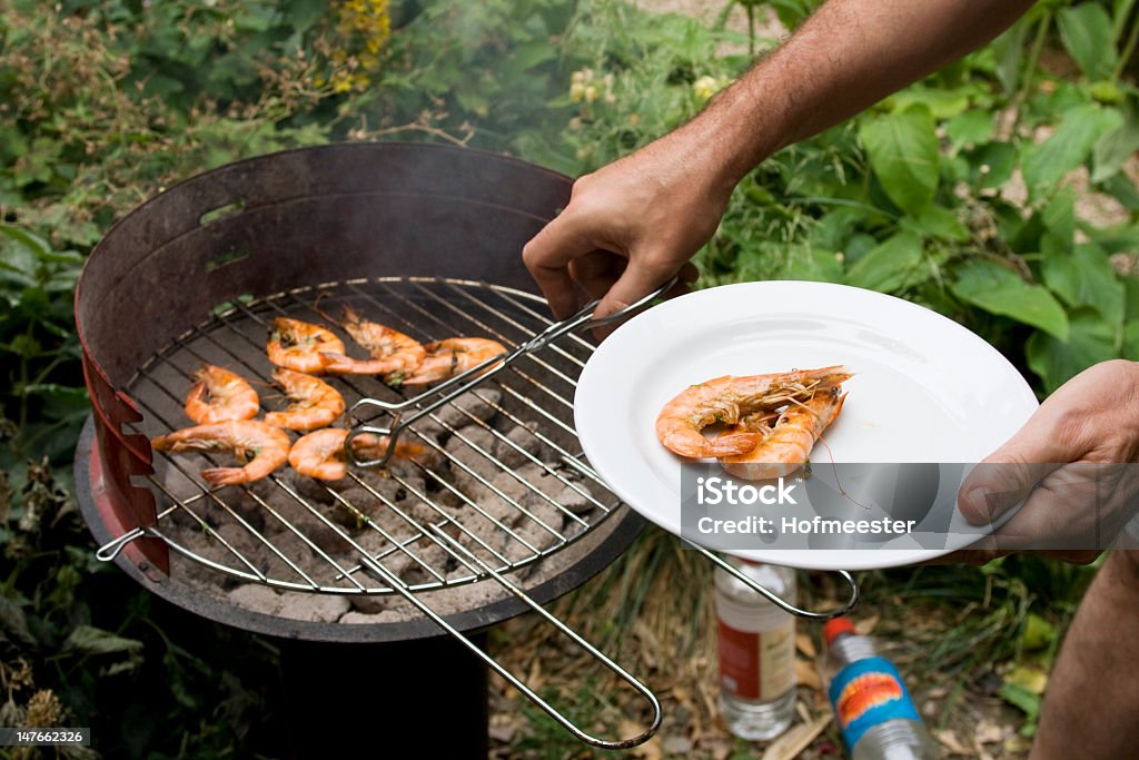 barbecue in garden Barbecue in garden with fresh prawns. Man puts prawns on plate. Focus on prawns on plate. Barbecue - Meal Stock Photo