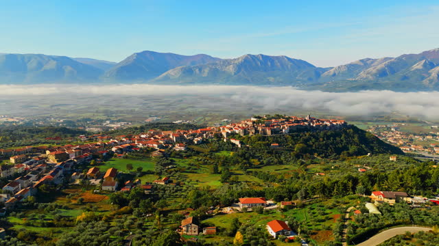 Atena Lucana. Fog moving over residential buildings in town on green landscape. Italy