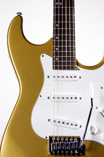 A metallic gold colored electric guitar isolated on a white background in the vertical format with copy space.