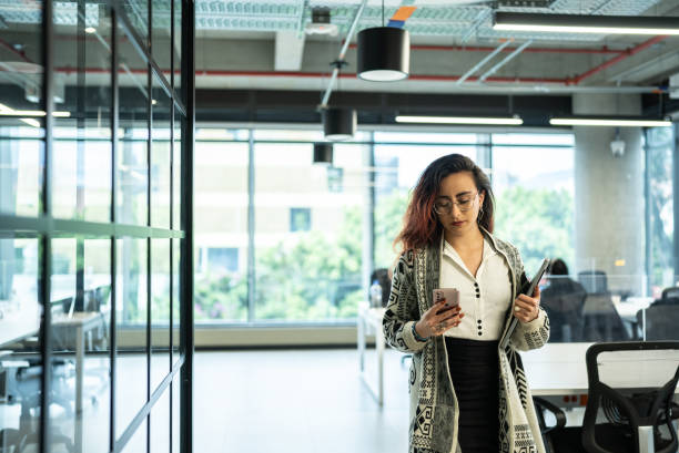 istock Young businesswoman walking through office using mobile phone 1476640768