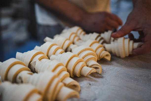 Baker man putting shaped croissants on tray after being rolled up