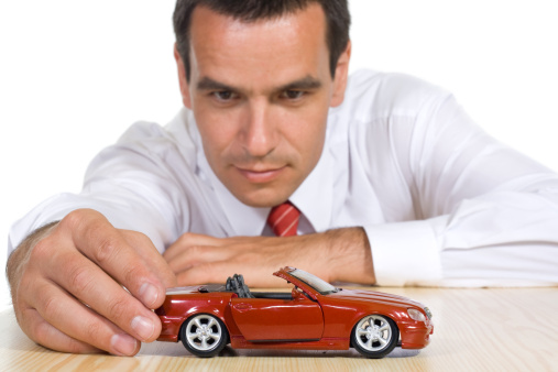 Businessman playing with a red toy car - isolated