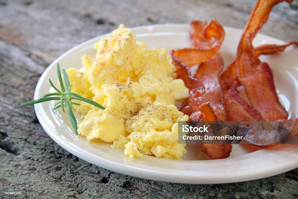 Bacon and scrambled eggs on a plate  Scrambled eggs with crispy bacon on a plate, and garnished with a fresh sprig of Rosemary. Bacon Stock Photo