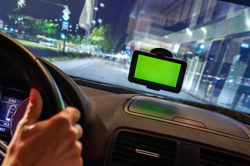 Driver driving car through city center at night time while using GPS navigator with green screen