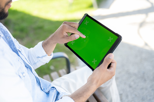 Man sitting in park and using digital tablet, pressing on green touch screen