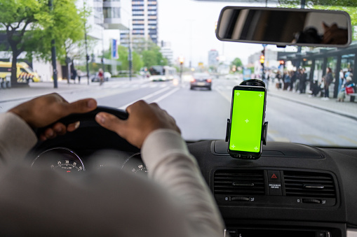 Person using GPS navigation on smartphone with chroma key green screen while driving car in city