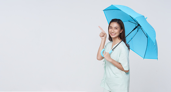 Happy smiling Asian woman standing and holding blue umbrella and pointing finger to isolated on white copy space background, life insurance and protection concept.