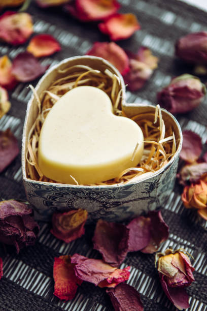 istock Solid Body cream bar in a heart shape gift box on black background, decorated with dry rose flower petals indoors. 1476664678
