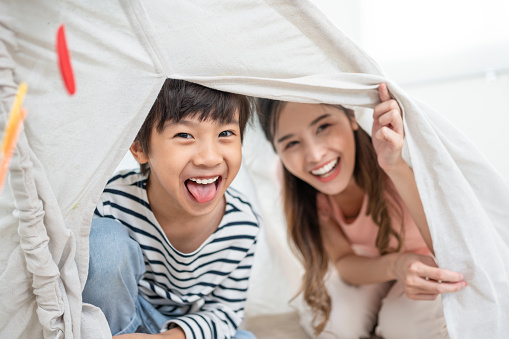 Happy mother and little son playing together in tent for children in living room at home