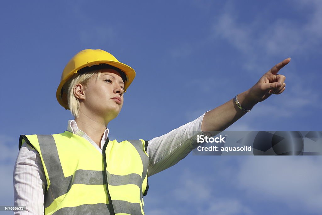 Donna che indica in un cappello duro e gilet di sicurezza. - Foto stock royalty-free di Adulto