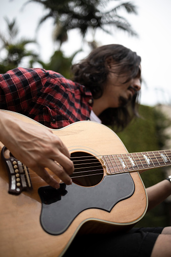 Caucasian long haired man playing yellow acoustic guitar on his backyard, wearing checkered shirt