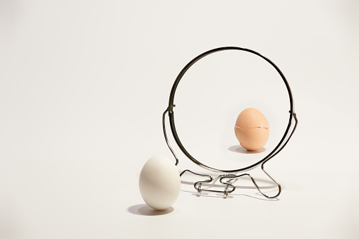 White and broken, cracked eggs reflected in the mirror on the white background.