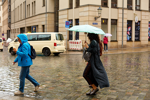 People with umbrellas run through a European city in the rain. Dresden, Germany - 05.20.2019