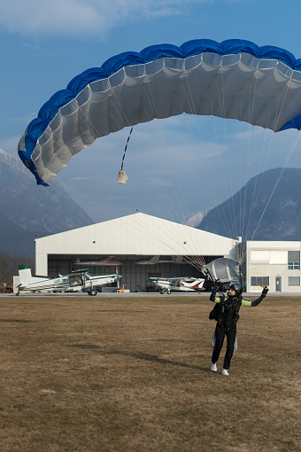 A female skydiver has jumped with a parachute and after the jump she picks up the parachute and carries it to the plane at the airport. She is happy and satisfied with the jump.