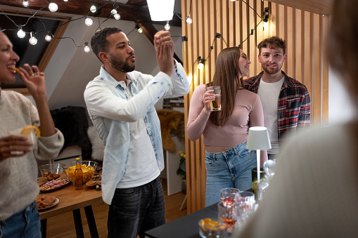 Two generations have a party at home with their partners, friends celebrate, sing, dance to music, sing karaoke on a mobile phone, have fun, drink alcoholic and non-alcoholic drinks A multi-racial society.