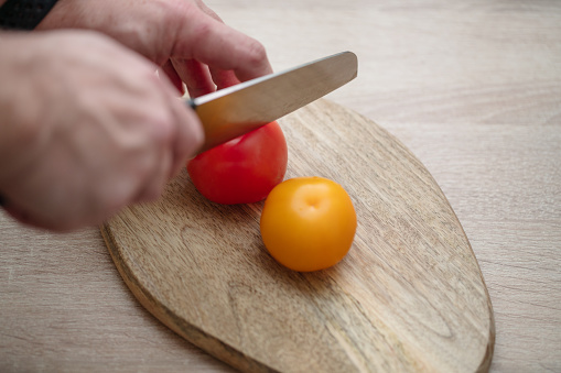Close-up shot of male hands chipping tomatoes on cutting board