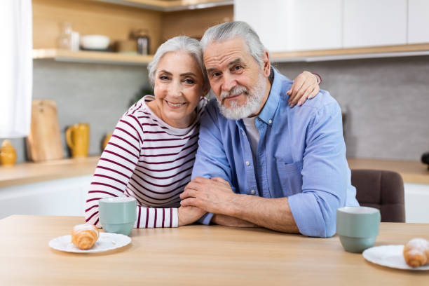 portrait of happy senior spouses posing at table in kitchen - two parent family indoors home interior domestic kitchen imagens e fotografias de stock