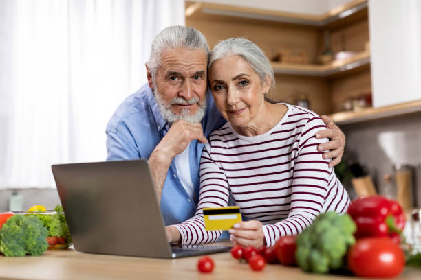 online shopping. elderly spouses posing with laptop and credit card in kitchen - two parent family indoors home interior domestic kitchen imagens e fotografias de stock