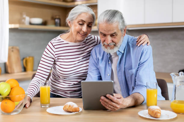 szczęśliwa para seniorów przeglądająca internet na tablecie cyfrowym podczas śniadania w kuchni - domestic kitchen family couple coffee zdjęcia i obrazy z banku zdjęć