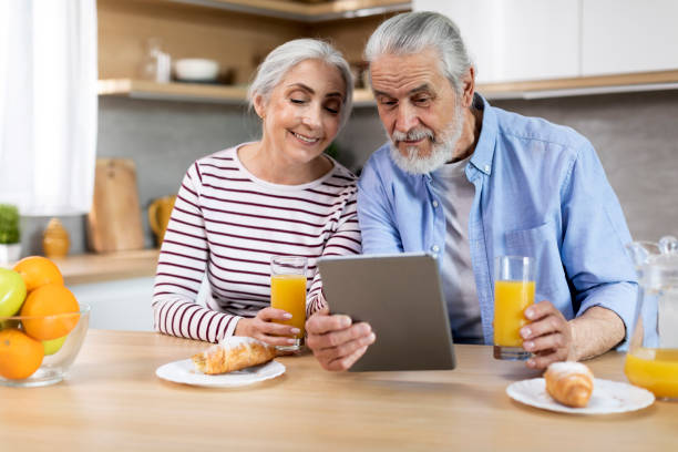 married elderly couple using digital tablet while having breakfast in kitchen together - two parent family indoors home interior domestic kitchen imagens e fotografias de stock