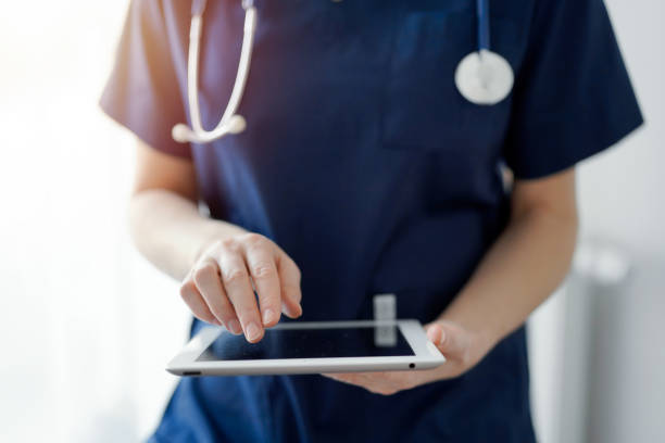 istock Doctor woman using tablet computer while standing near panorama window in clinic, close up. Physician or surgeon at work. Medicine concept 1476711609