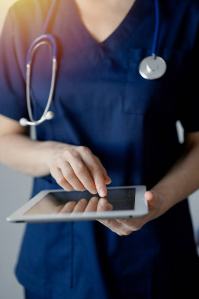 istock Doctor woman using tablet computer while standing near panorama window in clinic, close up. Physician or surgeon at work. Medicine concept 1476711623